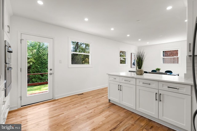 kitchen with multiple ovens, white refrigerator, light hardwood / wood-style flooring, and white cabinetry