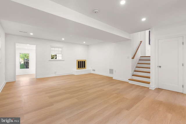 unfurnished living room with light wood-type flooring and brick wall