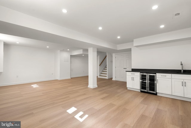 bar featuring white cabinets, light hardwood / wood-style floors, sink, and beverage cooler