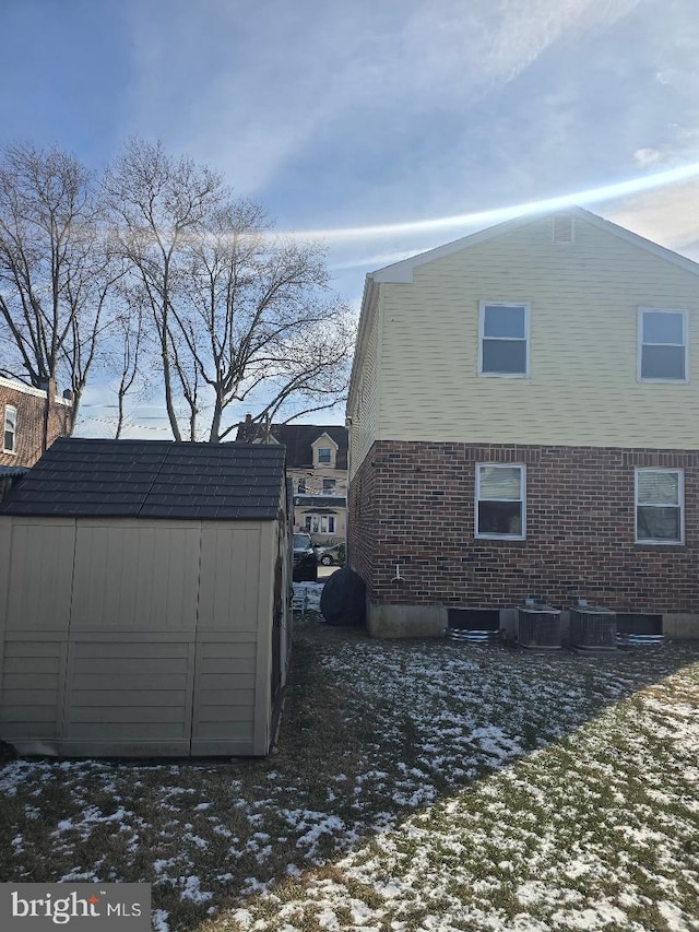 snow covered property with cooling unit and a storage unit