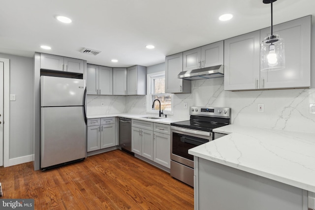 kitchen with light stone countertops, appliances with stainless steel finishes, dark hardwood / wood-style flooring, sink, and pendant lighting