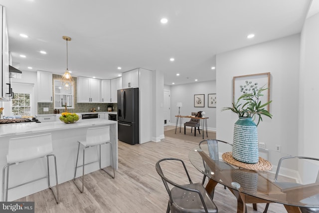 kitchen featuring white cabinetry, black appliances, kitchen peninsula, pendant lighting, and light hardwood / wood-style flooring