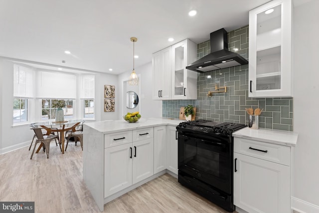 kitchen featuring black gas range oven, kitchen peninsula, decorative backsplash, wall chimney exhaust hood, and white cabinets