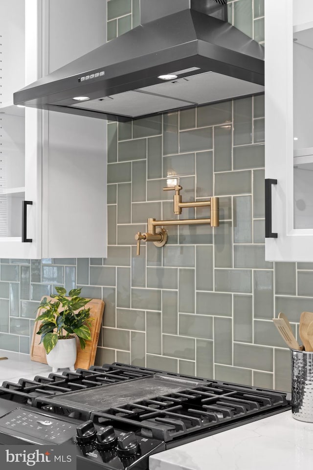 details featuring gas range, backsplash, range hood, and light stone countertops