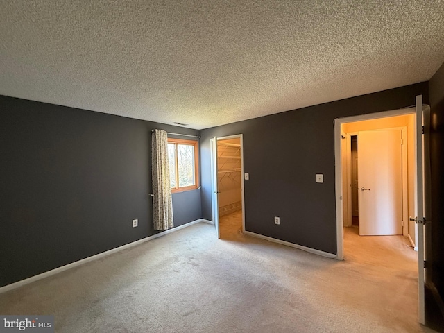 unfurnished bedroom with light colored carpet, a spacious closet, a textured ceiling, and a closet