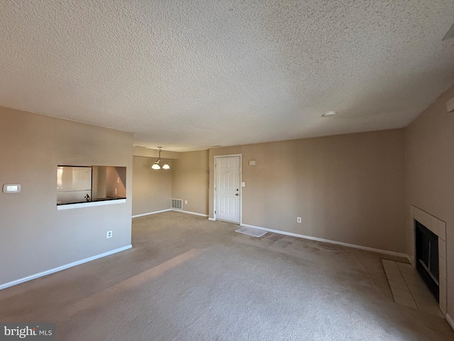 unfurnished living room with carpet flooring, a textured ceiling, an inviting chandelier, and a tile fireplace