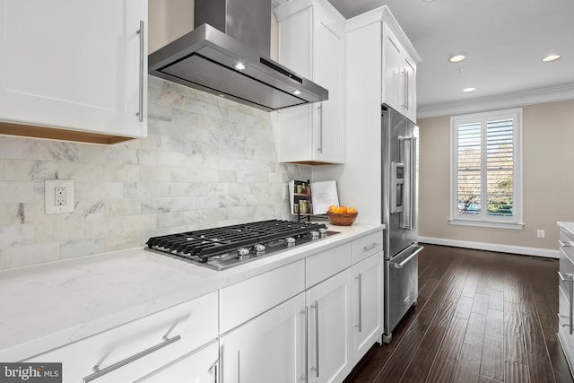 kitchen featuring crown molding, wall chimney range hood, stainless steel appliances, decorative backsplash, and white cabinets