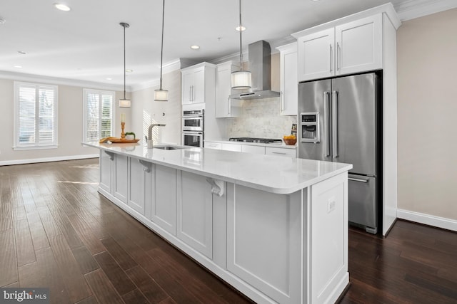 kitchen with white cabinetry, decorative light fixtures, a large island with sink, stainless steel appliances, and wall chimney range hood