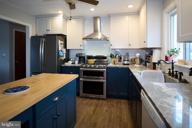 kitchen with wall chimney exhaust hood, white cabinetry, blue cabinets, and appliances with stainless steel finishes