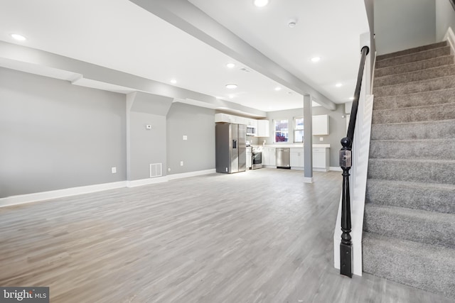 basement with stainless steel refrigerator with ice dispenser and light hardwood / wood-style flooring