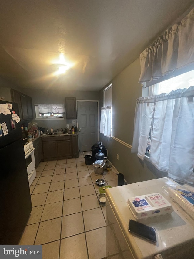 kitchen featuring black refrigerator, light tile patterned flooring, and white gas range oven