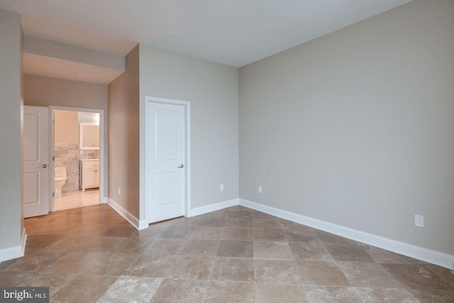 unfurnished bedroom featuring ensuite bathroom and baseboards