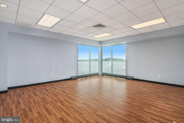 empty room with a paneled ceiling, a water view, and wood-type flooring