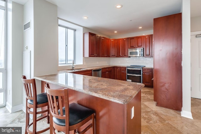 kitchen featuring sink, stainless steel appliances, light stone counters, kitchen peninsula, and a breakfast bar