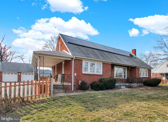 view of front facade featuring brick siding, a porch, a front yard, roof mounted solar panels, and fence