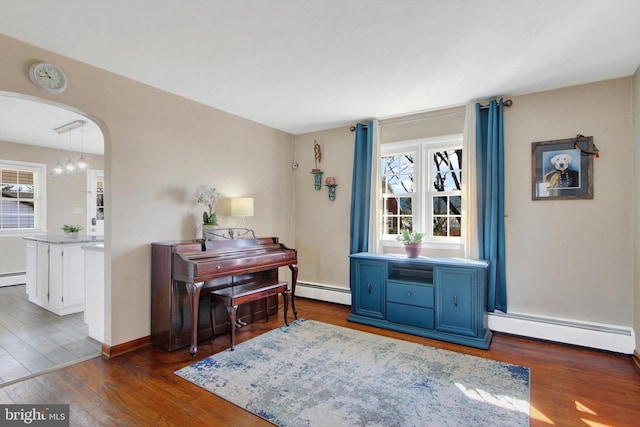 living area featuring a baseboard heating unit, wood finished floors, plenty of natural light, and arched walkways