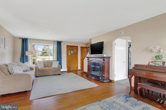 living room featuring a baseboard radiator, arched walkways, wood finished floors, and a glass covered fireplace