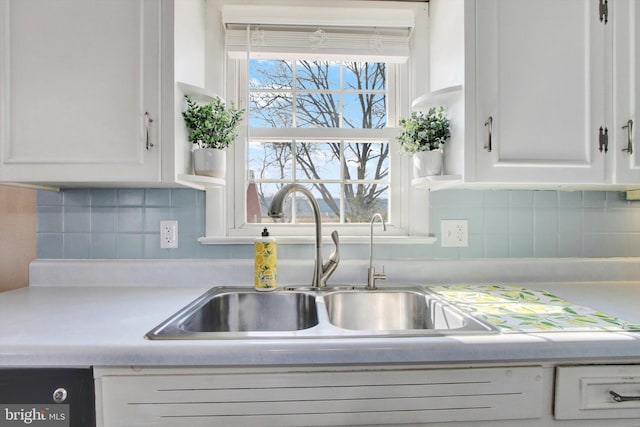 kitchen with light countertops, tasteful backsplash, a sink, and white cabinetry