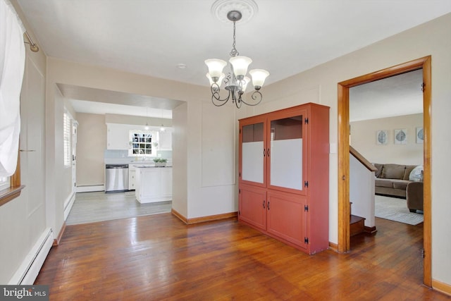 unfurnished dining area with a chandelier, baseboard heating, a baseboard radiator, and wood finished floors