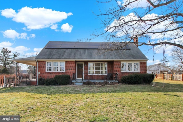 view of front of house featuring a front yard, brick siding, fence, and solar panels