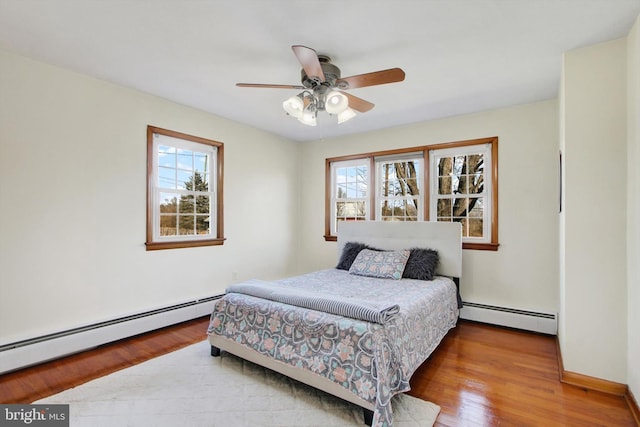 bedroom with a baseboard heating unit, multiple windows, and wood finished floors