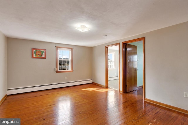 spare room featuring a baseboard radiator, baseboards, and hardwood / wood-style flooring