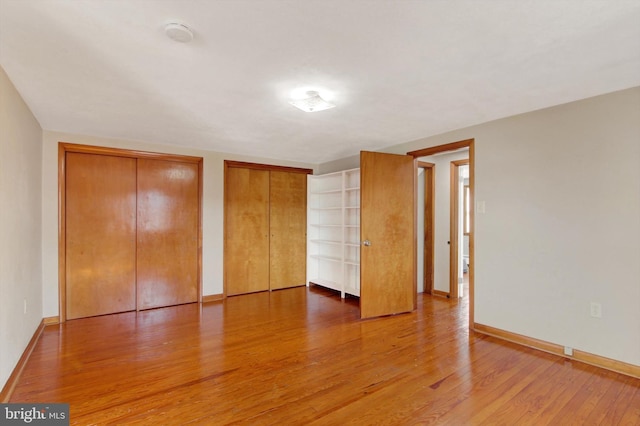 unfurnished bedroom featuring multiple closets, baseboards, and wood finished floors