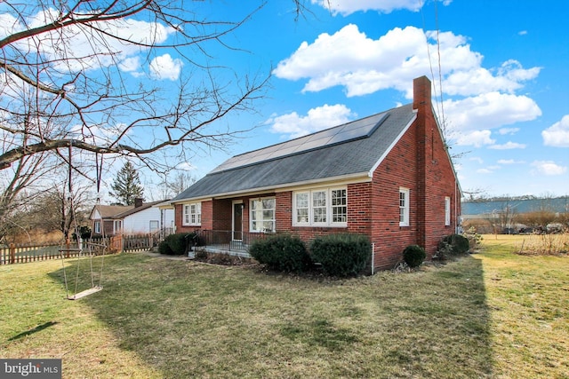 view of front facade featuring solar panels, a chimney, fence, a front lawn, and brick siding