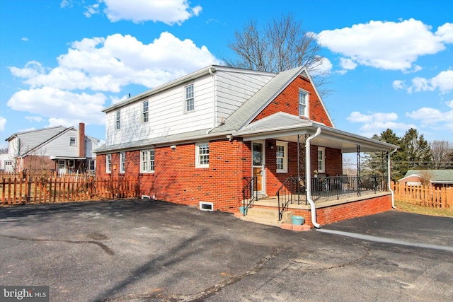 view of side of home featuring a porch, fence, and brick siding