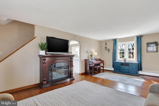 living room featuring arched walkways, baseboard heating, a baseboard heating unit, a glass covered fireplace, and wood finished floors