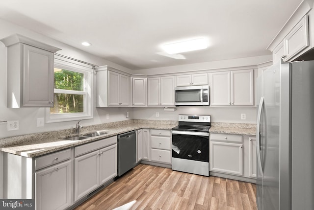 kitchen featuring sink, light hardwood / wood-style flooring, gray cabinets, light stone countertops, and appliances with stainless steel finishes