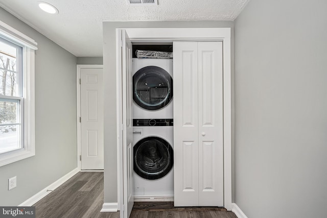 washroom featuring a textured ceiling, dark hardwood / wood-style floors, and stacked washer / dryer