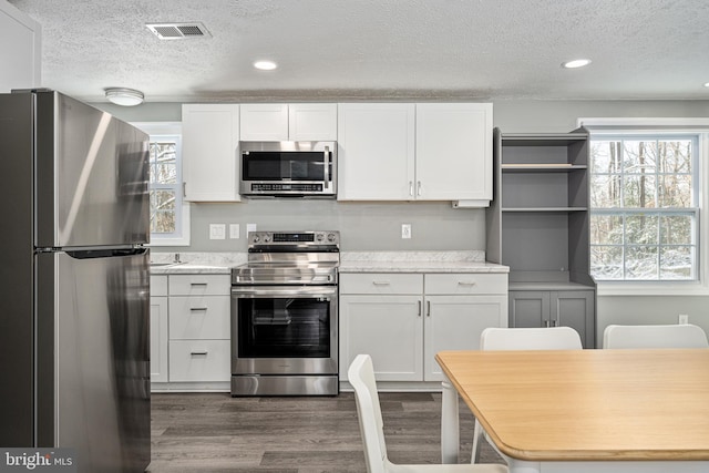 kitchen featuring dark wood-type flooring, white cabinets, a textured ceiling, light stone counters, and stainless steel appliances