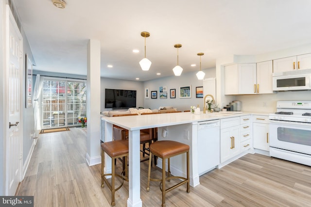 kitchen featuring kitchen peninsula, decorative light fixtures, white appliances, a kitchen bar, and white cabinets