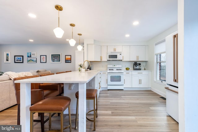 kitchen featuring white cabinetry, hanging light fixtures, a kitchen breakfast bar, kitchen peninsula, and white appliances