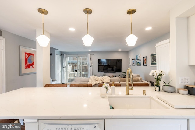 kitchen with light stone counters, sink, white cabinets, and pendant lighting