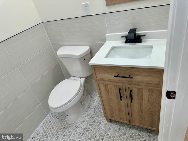 bathroom with toilet, vanity, tile patterned floors, and tile walls