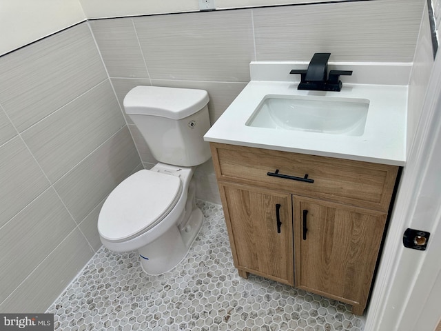 bathroom featuring tile patterned flooring, vanity, toilet, and tile walls