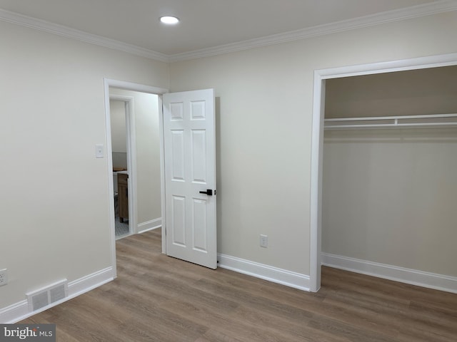 unfurnished bedroom featuring hardwood / wood-style flooring, crown molding, and a closet