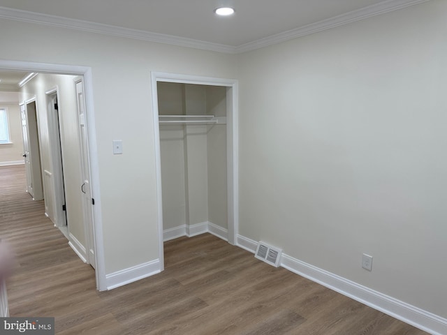 unfurnished bedroom featuring hardwood / wood-style flooring, crown molding, and a closet