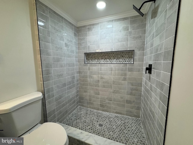 bathroom featuring a tile shower, toilet, and ornamental molding