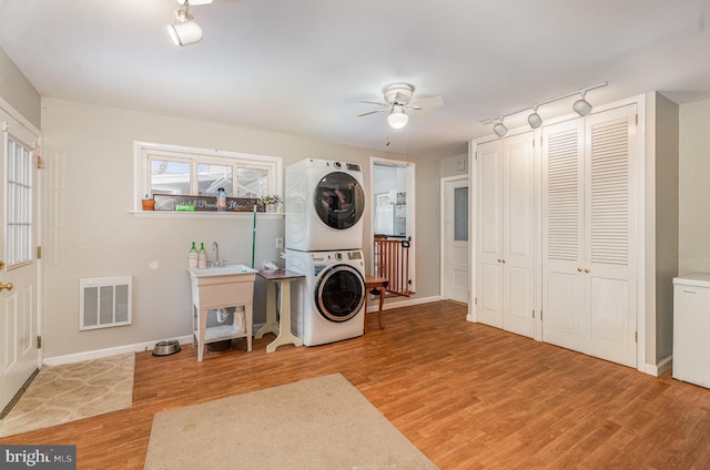 clothes washing area with stacked washer / drying machine, ceiling fan, and light wood-type flooring