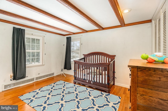 bedroom featuring hardwood / wood-style floors, a nursery area, and a baseboard heating unit