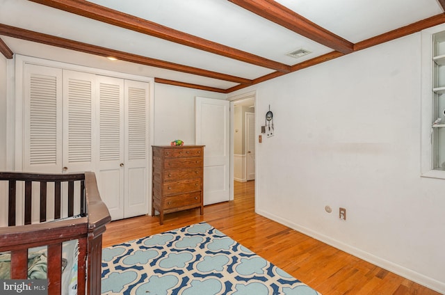 bedroom with beam ceiling, light hardwood / wood-style floors, a closet, and a nursery area