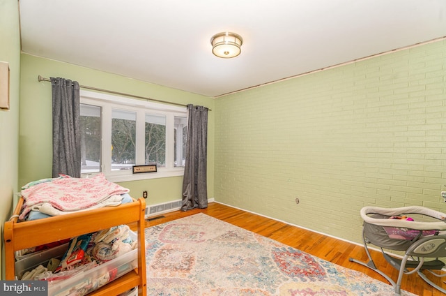 bedroom featuring wood-type flooring and brick wall