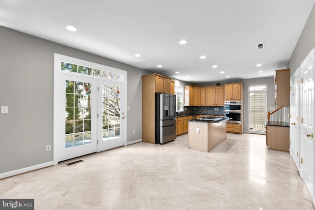 kitchen featuring dark countertops, a center island, baseboards, decorative backsplash, and appliances with stainless steel finishes