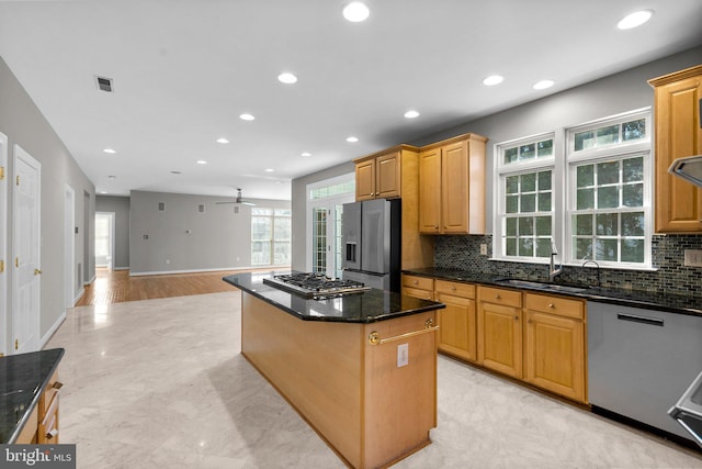 kitchen with visible vents, a kitchen island, dark stone counters, stainless steel appliances, and a sink