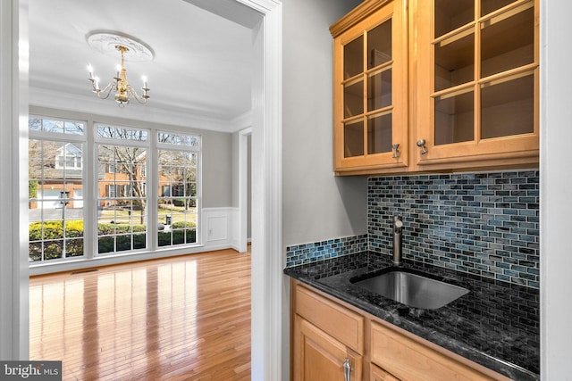 kitchen with a sink, tasteful backsplash, wood finished floors, dark stone counters, and crown molding