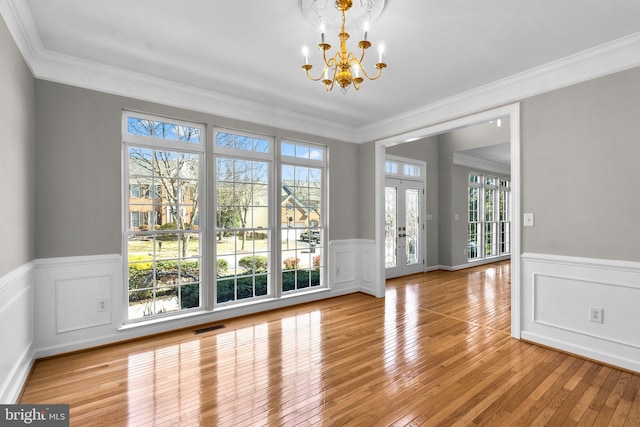 unfurnished dining area with visible vents, hardwood / wood-style flooring, french doors, wainscoting, and a chandelier