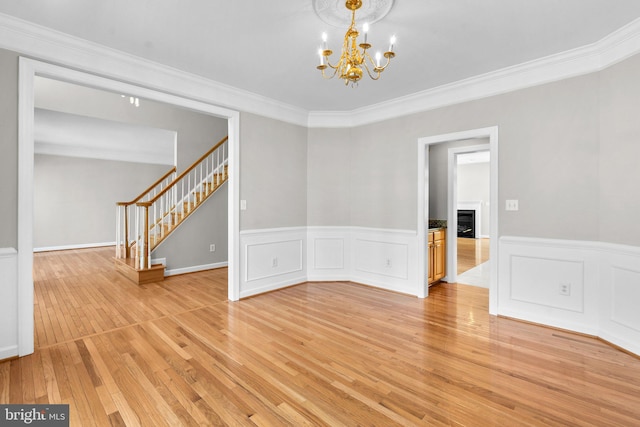 spare room featuring light wood finished floors, crown molding, stairs, a fireplace, and an inviting chandelier